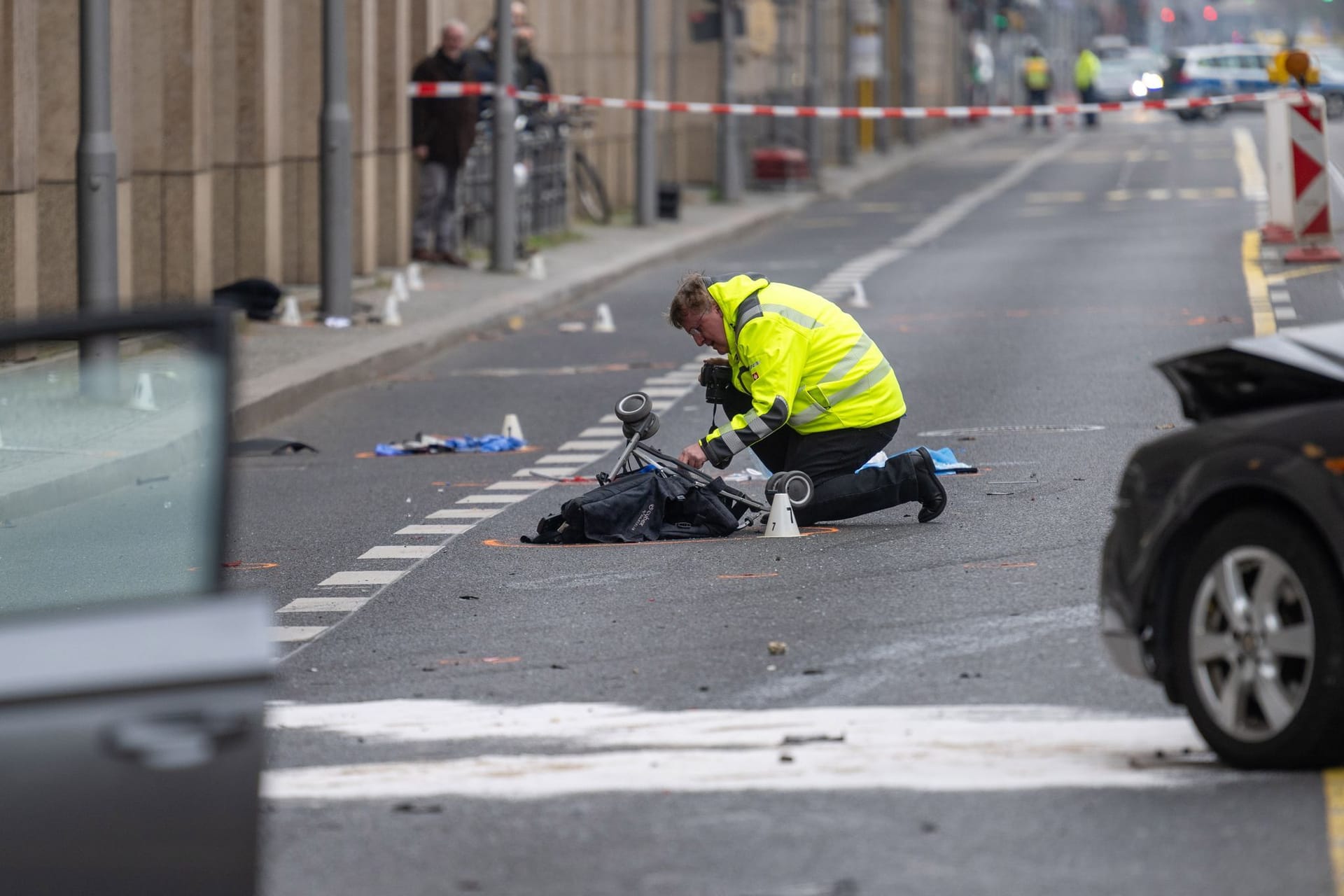 Ein Polizist kniet an einer Unfallstelle in der Leipziger Straße an einem Kinderwagen.