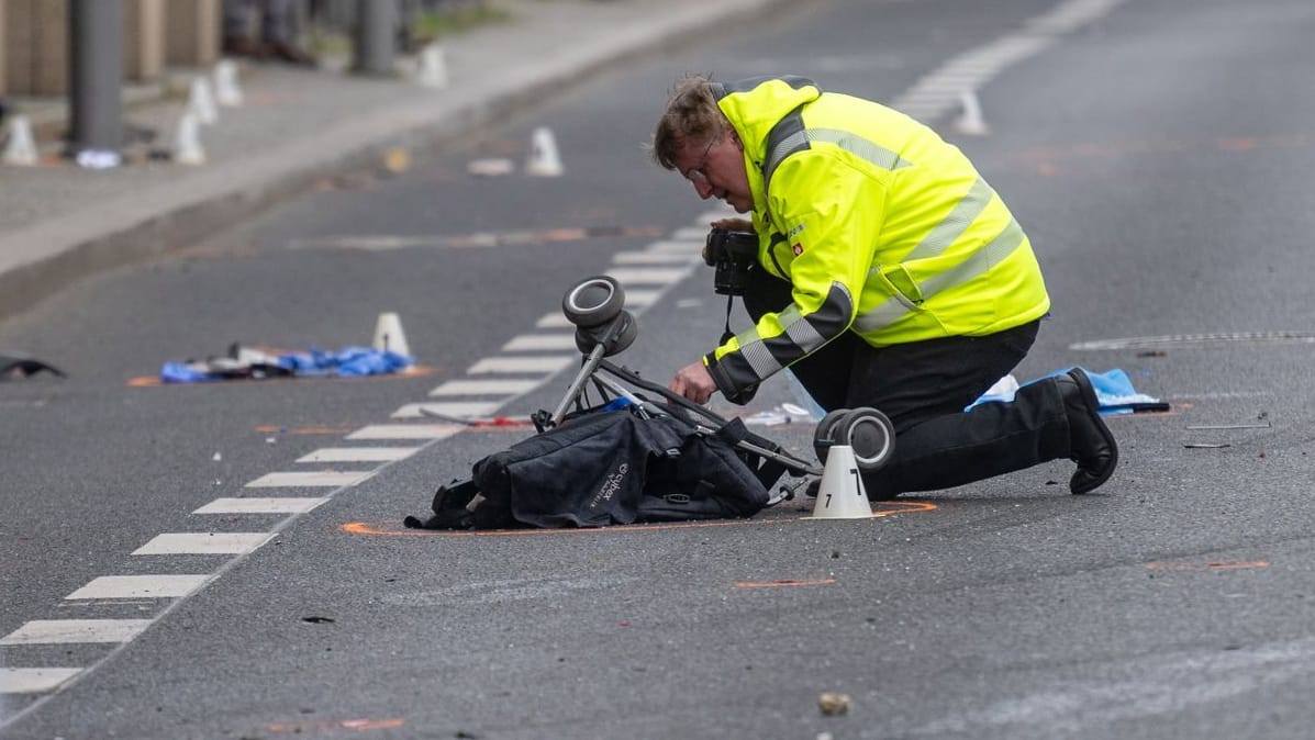 Ein Polizist kniet an einer Unfallstelle in der Leipziger Straße an einem Kinderwagen.