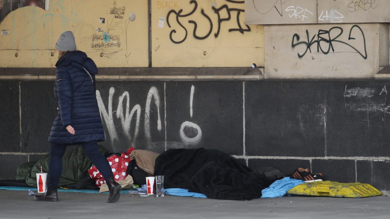 Eine Frau geht an zwei Obdachlosen vorbei, die unter einer Brücke am Dammtor-Bahnhof schlafen.
