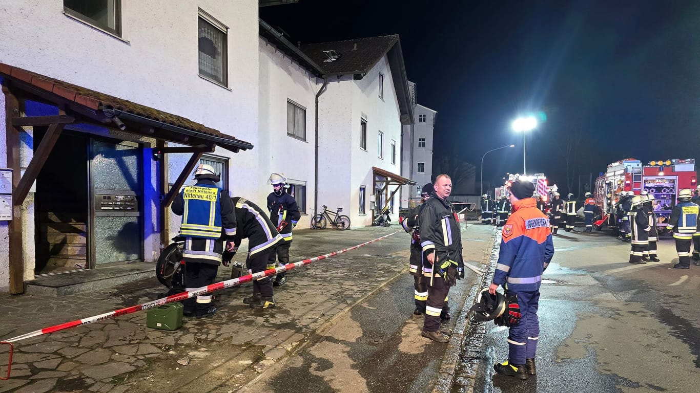 Einsatzkräfte der Feuerwehr stehen nach einem Brand vor einem Wohnkomplex in der Oberpfalz. Bei dem Brand sind mehr als 30 Menschen durch Rauch verletzt worden.