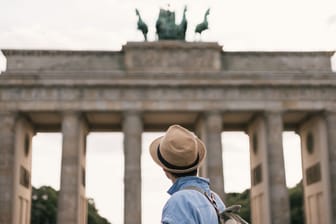 Ein Mann steht vor dem Brandenburger Tor in Berlin (Symbolbild): Eine Plattform hat ausgewertet, wie viel Geld man braucht, um in Berlin über die Runden zu kommen.