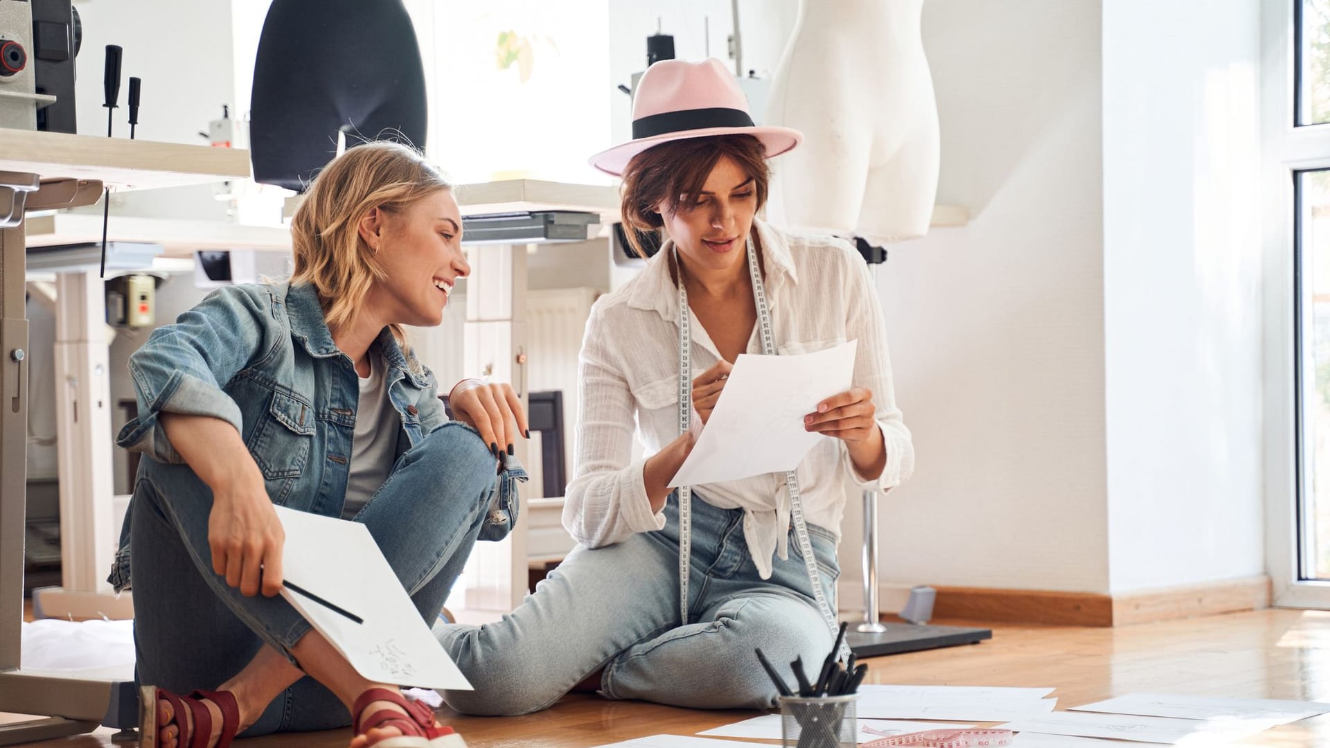 Zwei junge Frauen sitzen auf dem Boden in ihrem Atelier und planen die nächsten Arbeitsschritte