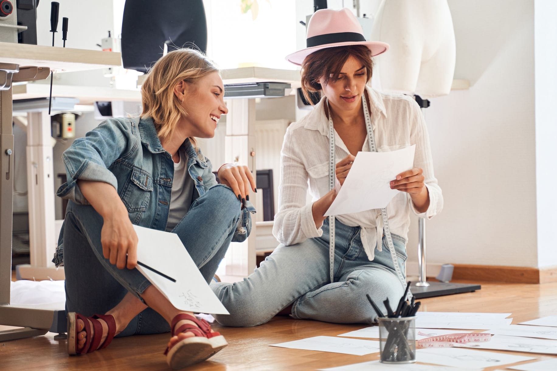 Zwei junge Frauen sitzen auf dem Boden in ihrem Atelier und planen die nächsten Arbeitsschritte