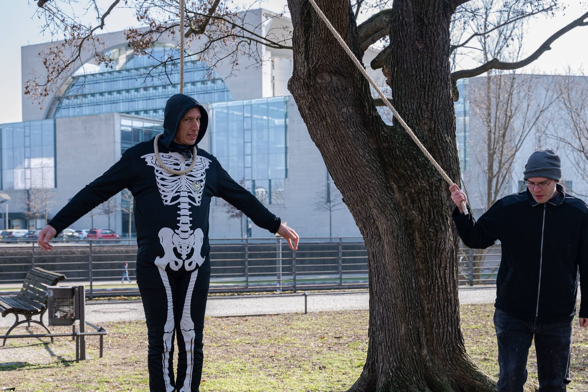 07.03.2024, Berlin, Deutschland, Europa - Der deutsche Klimaaktivist Wolfgang Wolli Metzeler-Kick traegt ein Skelettkostuem und steht mit einer Schlinge um den Hals auf einem schmelzenden Eisblock neben einem Baum, waehrend im Hintergrund das Bundeskanzleramt zu sehen ist.