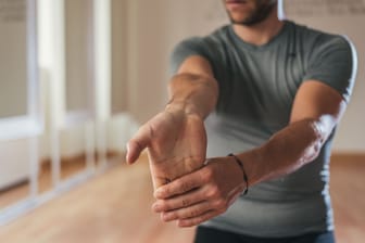 Ein Mann dehnt die Unterarmmuskeln: Ob sich das Karpaltunnelsyndrom allein mit Übungen behandeln lässt, ist fraglich. Sie können die Therapie jedoch unterstützen.