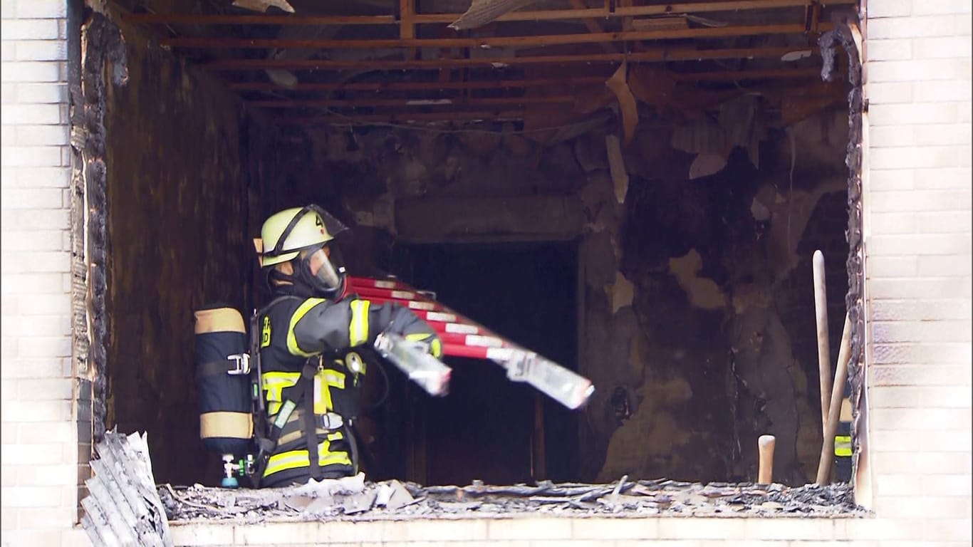 Feuerwehreinsatz in Dortmund: Ein Feuerwehrmann mit Atemschutz hebt eine Leiter in die ausgebrannten Wohnräume.