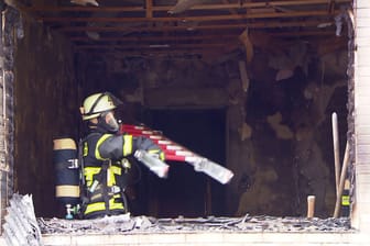 Feuerwehreinsatz in Dortmund: Ein Feuerwehrmann mit Atemschutz hebt eine Leiter in die ausgebrannten Wohnräume.