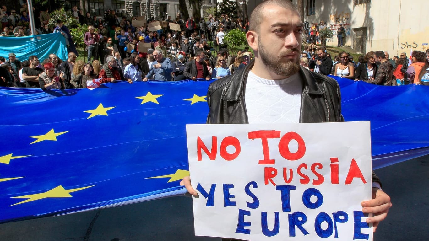 Protest in Tiflis: Ein Mann steht vor Demonstranten mit einer riesigen EU-Flagge vor dem Parlamentsgebäude.
