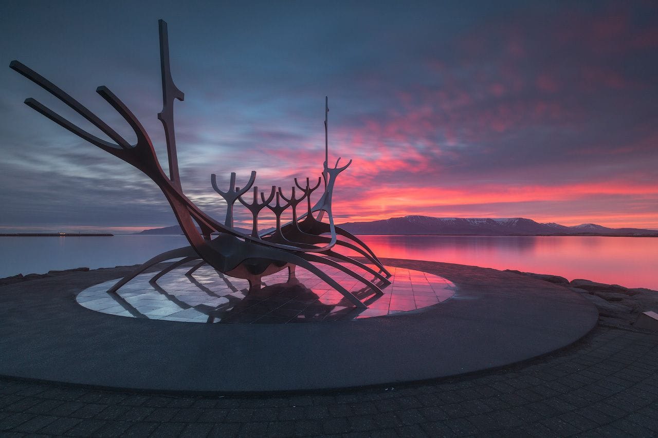 Küstenstraße Sæbraut in Reykjavik: Die Skulptur Sonnenfahrt des Künstlers Jón Gunnar Árnason liegt schwarz im Gegenlicht der aufgehenden Sonne.