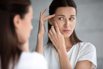 Eine Frau betrachtet ihr Gesicht im Spiegel: Rufen Medikamente Pigmentflecken hervor, kann das beunruhigen.