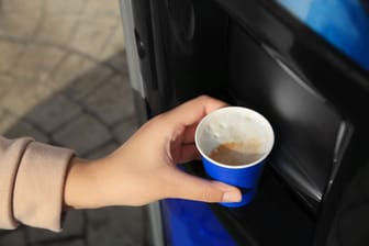 Woman taking paper cup with coffee from vending machine outdoors, closeup