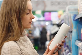 Eine Frau liest das Etikett eines Kosmetikprodukts