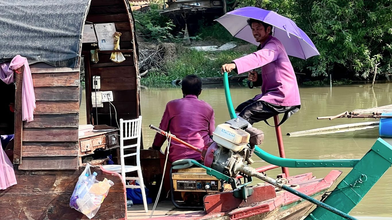 Menschen auf einem Boot auf dem Pa Sak River schützen sich bei Ayutthaya mit Sonnenschirmen vor der Sonneneinstrahlung.