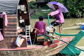 Menschen auf einem Boot auf dem Pa Sak River schützen sich bei Ayutthaya mit Sonnenschirmen vor der Sonneneinstrahlung.