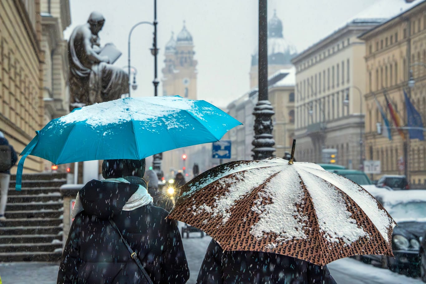 Zwei Menschen schützen sich mit Regenschirmen gegen Schneefall in München (Archivbild): Die Landeshauptstadt wird von der weißen Pracht aber wohl verschont.