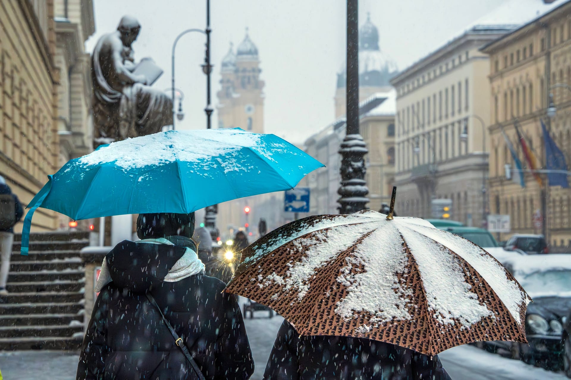 Zwei Menschen schützen sich mit Regenschirmen gegen Schneefall in München (Archivbild): Die Landeshauptstadt wird von der weißen Pracht aber wohl verschont.