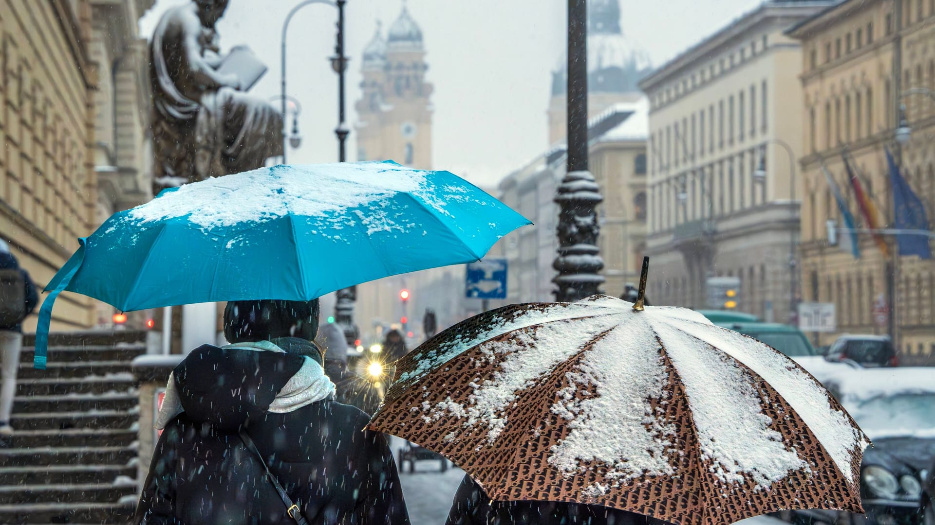 Zwei Menschen schützen sich mit Regenschirmen gegen Schneefall in München (Archivbild): Die Landeshauptstadt wird von der weißen Pracht aber wohl verschont.