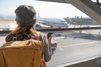 Happy Asian tourist uses mobile smartphone with travel backpack while waiting for flight in airport