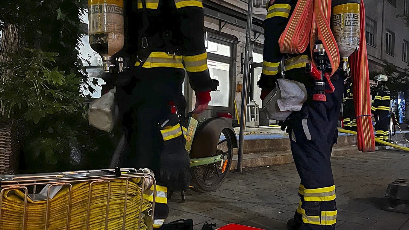Zwei Feuerwehrleute stehen vor dem Stammhaus von Feinkost Käfer: Der Schaden beläuft sich nach ersten Schätzungen auf rund 50.000 Euro.