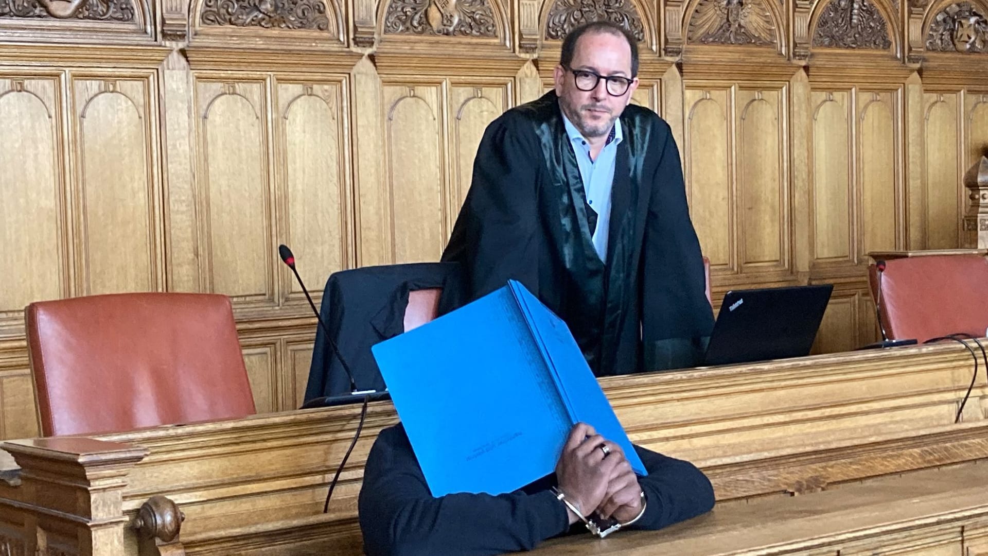 Der Angeklagte sitzt in einem Saal des Landgerichts, hinter ihm steht sein Verteidiger Alexander Gellinger.