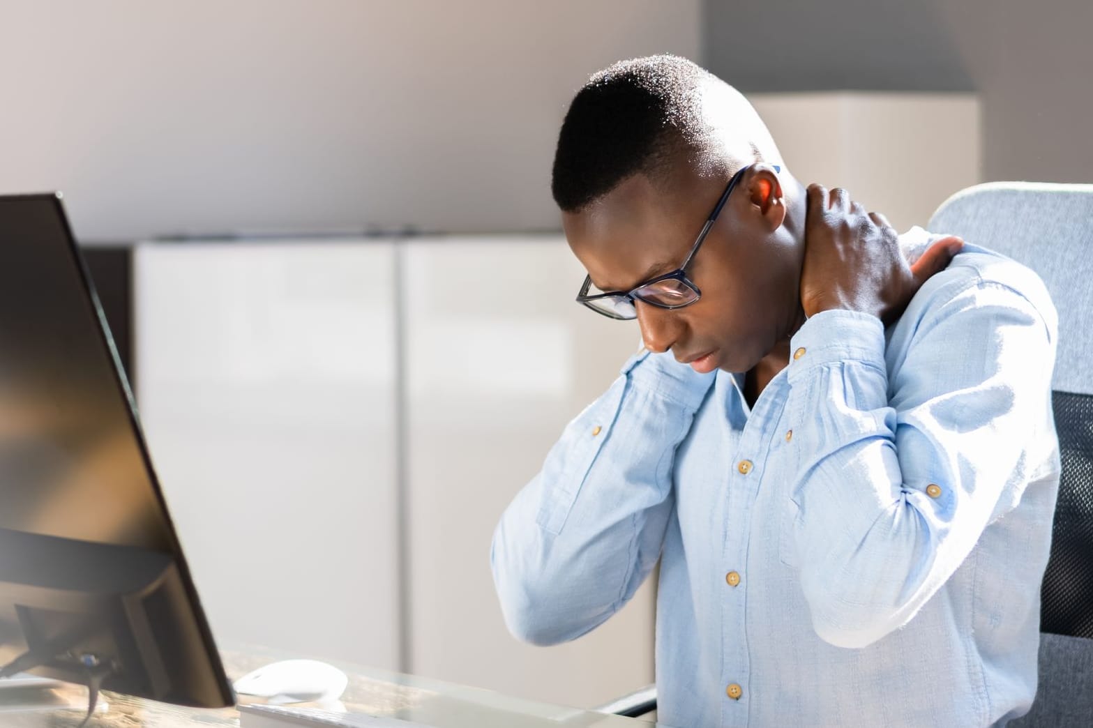 Ein am Computer sitzender Mann greift sich in den Nacken