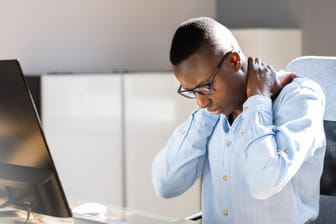 Ein am Computer sitzender Mann greift sich in den Nacken