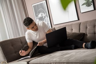 Ein Mann sitzt mit Laptop auf einem Sofa