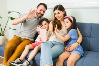 Familie, Mutter, Vater und zwei Kinder, sitzen auf dem Sofa und machen ein Selfie