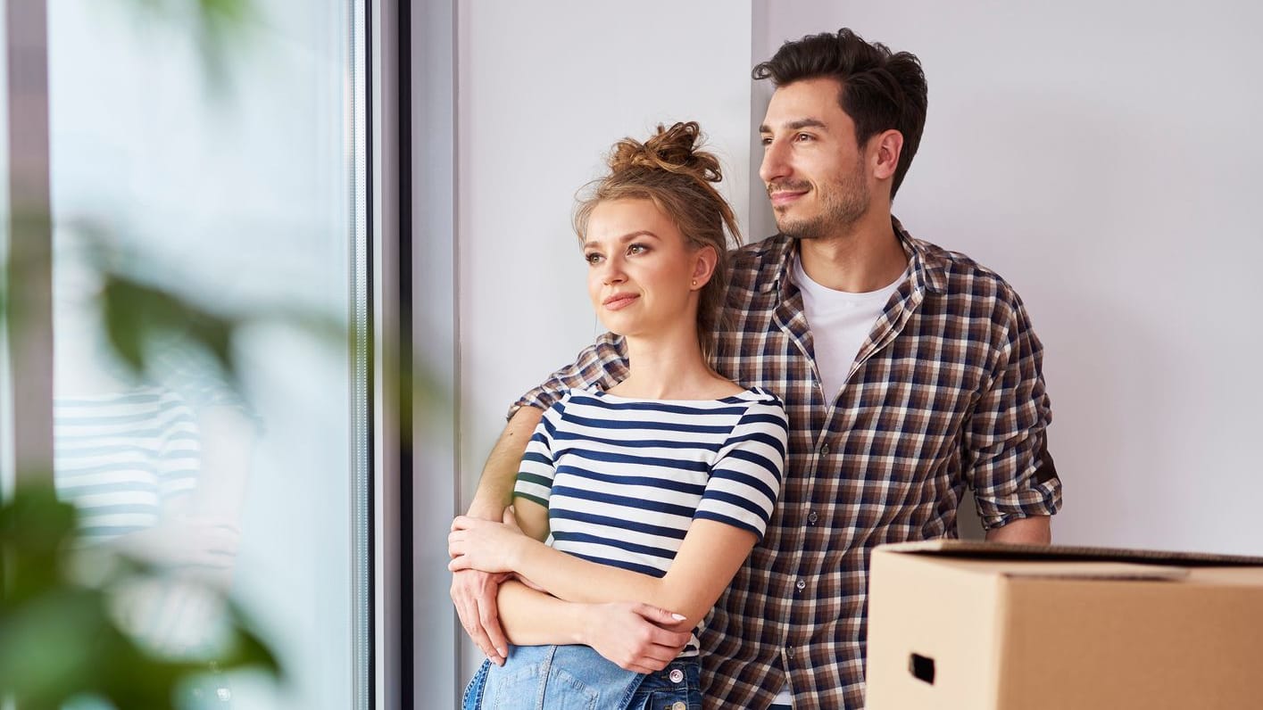 Paar blickt aus dem Fenster: Für ein Eigenheim braucht es in der Regel eine Baufinanzierung.