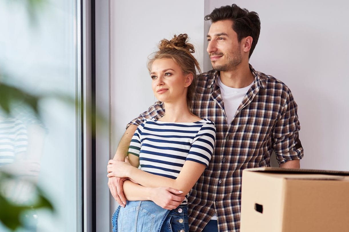 Paar blickt aus dem Fenster: Für ein Eigenheim braucht es in der Regel eine Baufinanzierung.