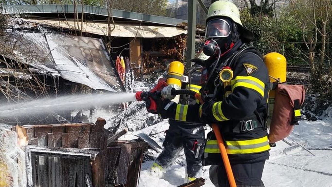 Ein Feuerwehrmann mit Atemschutz löscht eine Gartenhütte mit Löschschaum in München-Sendling.