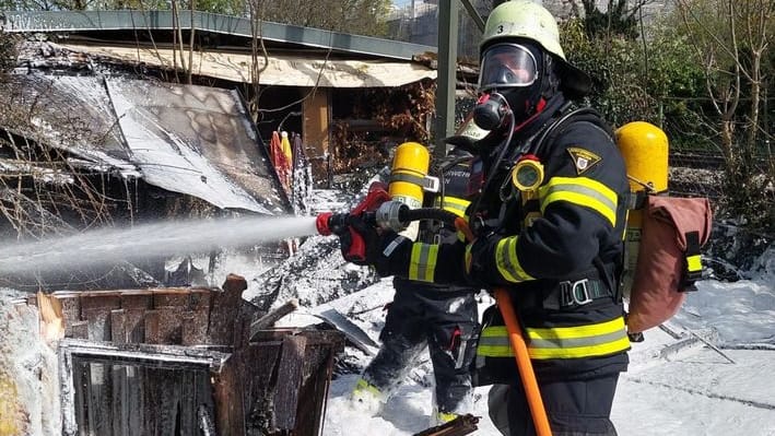 Ein Feuerwehrmann mit Atemschutz löscht eine Gartenhütte mit Löschschaum in München-Sendling. Ein Feuerwehrmann mit Atemschutz löscht eine Gartenhütte mit Löschschaum in München-Sendling.