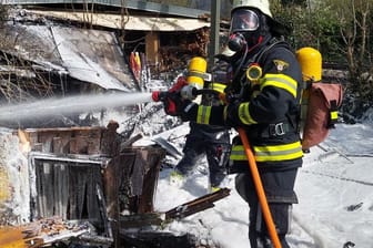 Ein Feuerwehrmann mit Atemschutz löscht eine Gartenhütte mit Löschschaum in München-Sendling.