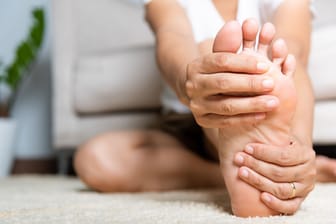 Eine Frau umfasst ihren Fuß: Dornwarzen gehen oft mit Schmerzen einher. Wie lassen sie sich entfernen?
