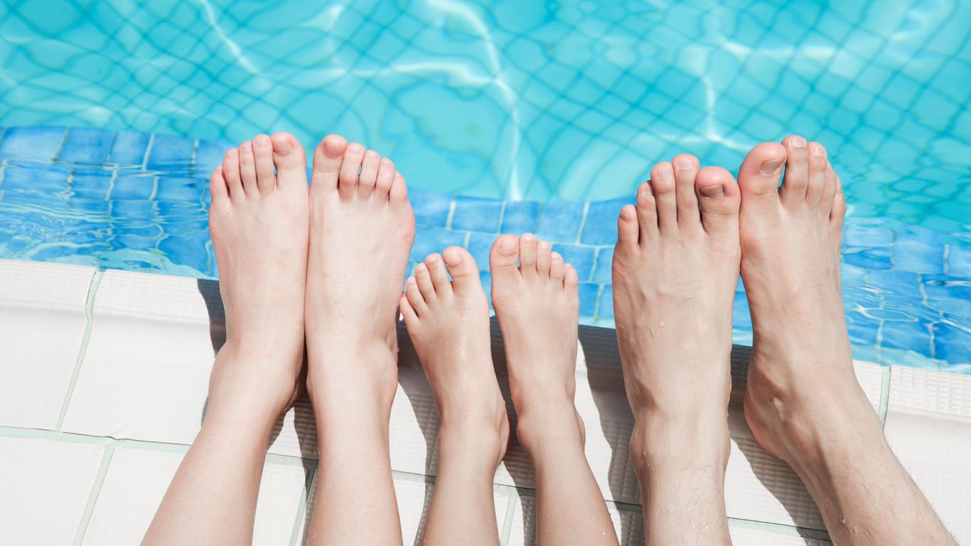 Füße von zwei Erwachsenen und einem Kind am Rand eines Schwimmbeckens