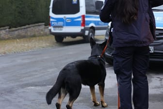 Polizeibeamter mit Hund stehen in der Nähe eines Gebäudes, das durchsucht wird: Unter anderem in Köln sucht die Polizei nach Beweismitteln.