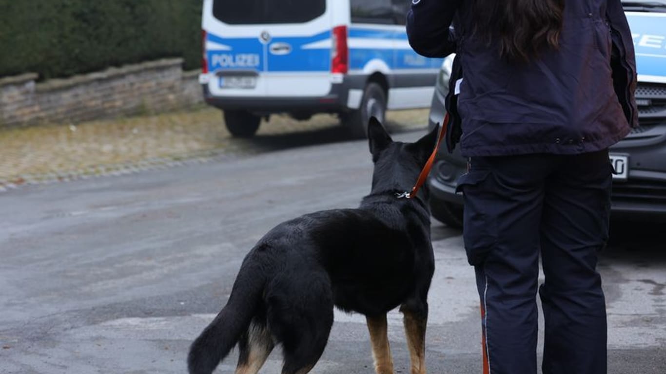 Polizeibeamter mit Hund stehen in der Nähe eines Gebäudes, das durchsucht wird: Unter anderem in Köln sucht die Polizei nach Beweismitteln.