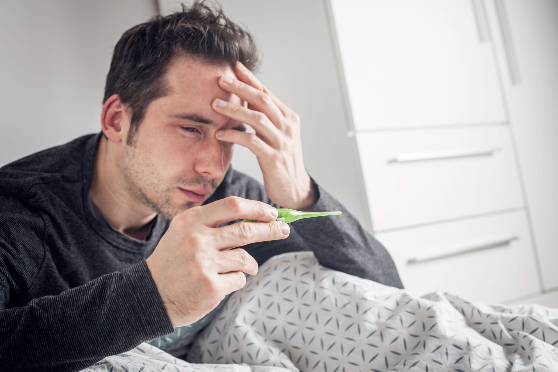 Junger Mann schaut auf das Fieberthermometer