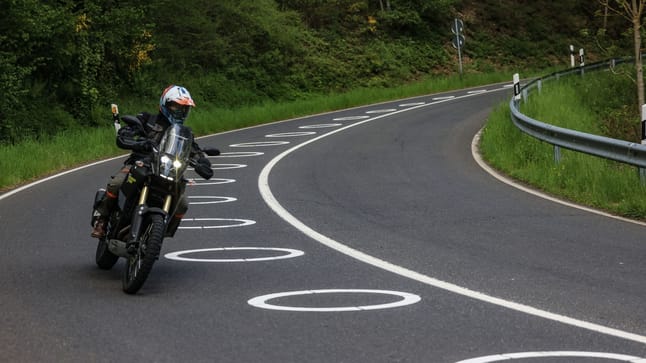 ein motorradfahrer faehrt bei vossenack durch eine serpentine mit aufgemalten kreisen auf der fahrbahn
