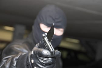 Ein maskierter Mann hält ein Messer in der Hand (Symbolbild): Der Lieferdienstfahrer blieb bei dem Überfall unverletzt.