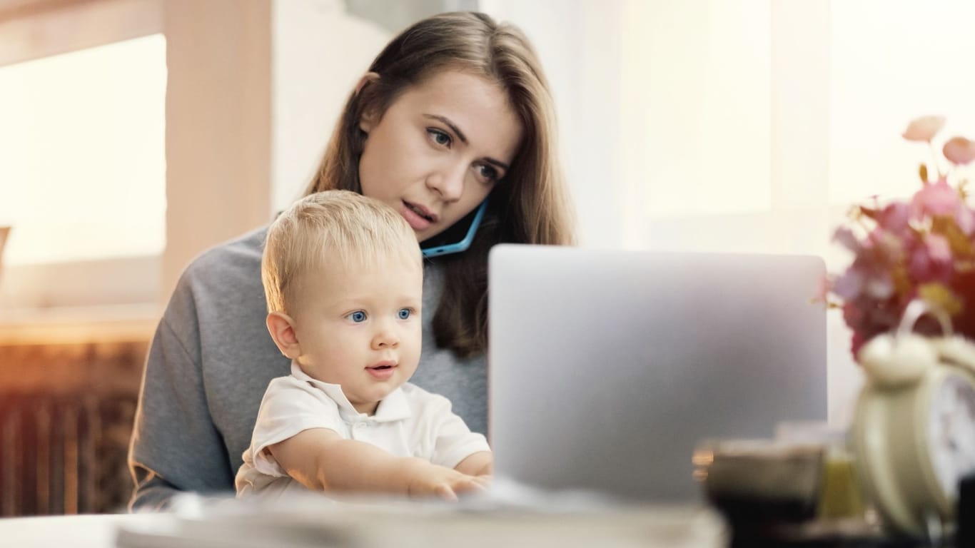 Frau mit Kind sitzt am Tisch und beide schauen auf einen Laptop