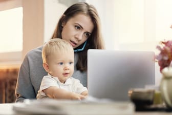 Frau mit Kind sitzt am Tisch und beide schauen auf einen Laptop