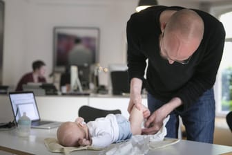 Ein junger Vater wickelt sein Kind auf einem Schreibtisch im Büro (Archivbild): Leibliche Väter möchten mehr Rechte haben, bekommen dann aber auch mehr Pflichten.
