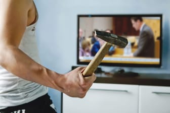 Mann mit Hammer vor dem Fernseher (Symbolbild): Die Zunahme der Gewalt gegen Amtsträger ist ein Alarmzeichen.
