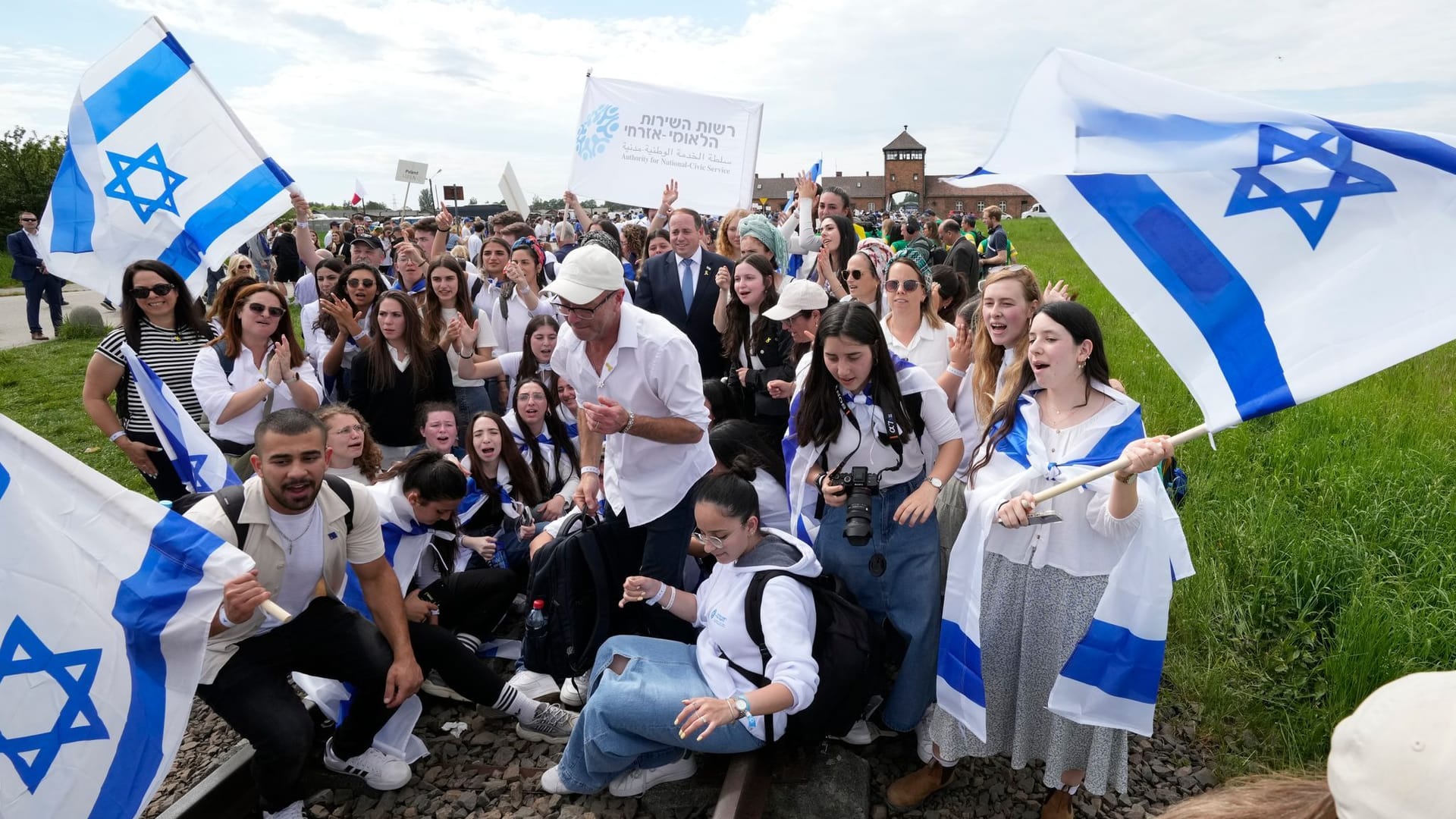 Polen, Oswiecim: Menschen stehen mit Fahnen vor dem ehemaligen deutschen Vernichtungslager Auschwitz-Birkenau, während der jährlichen Holocaust-Gedenkveranstaltung, dem "Marsch der Lebenden".