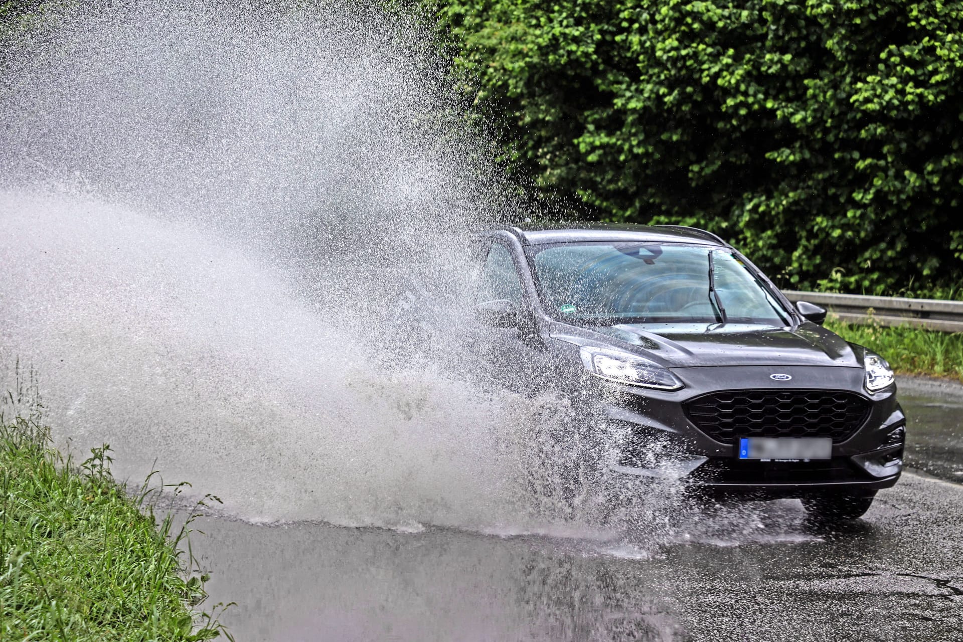 Überflutete Straßen bei Starkregen: Kurzfristige Überflutung einer Straße im Bereich einer Kurve mit gefährlichen Wassermassen, die von den Fahrzeugen aufgewirbelt werden und für Schrecksekunden sorgen.