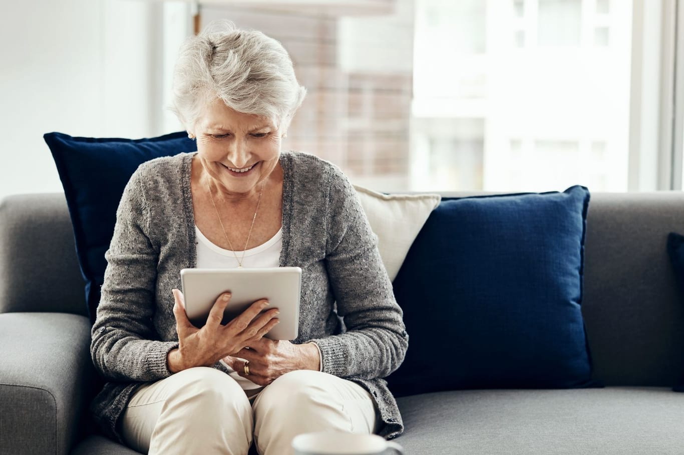 Ältere Frau blickt freudig auf ein Tablet: Wer weiß wie, kann sich mit ETFs entspannt eine Zusatzrente aufbauen.