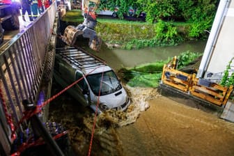 Bayern, Kastl: Feuerwehrleute und ein Bagger arbeiten daran, einen Kastenwagen aus den Überflutungen vor einer Brücke zu bergen.