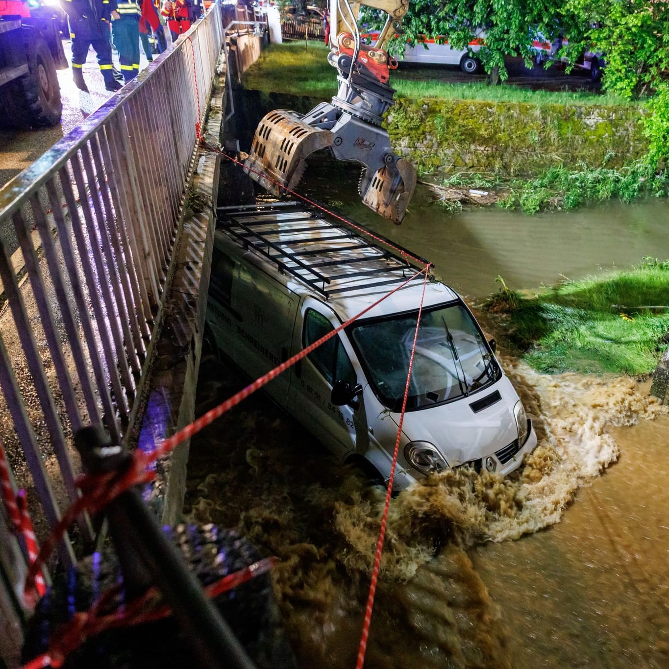 Bayern, Kastl: Feuerwehrleute und ein Bagger arbeiten daran, einen Kastenwagen aus den Überflutungen vor einer Brücke zu bergen.