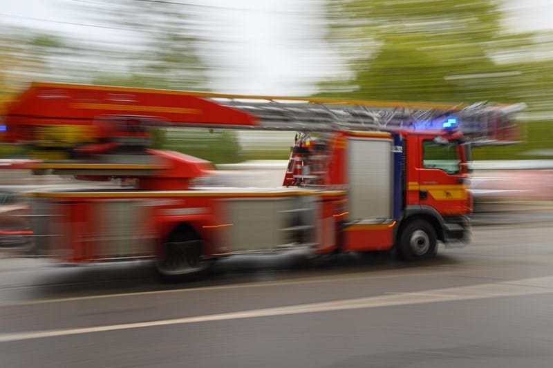 Ein Feuerwehrfahrzeug mit Drehleiter fährt in der Innenstadt zu einem Einsatz.